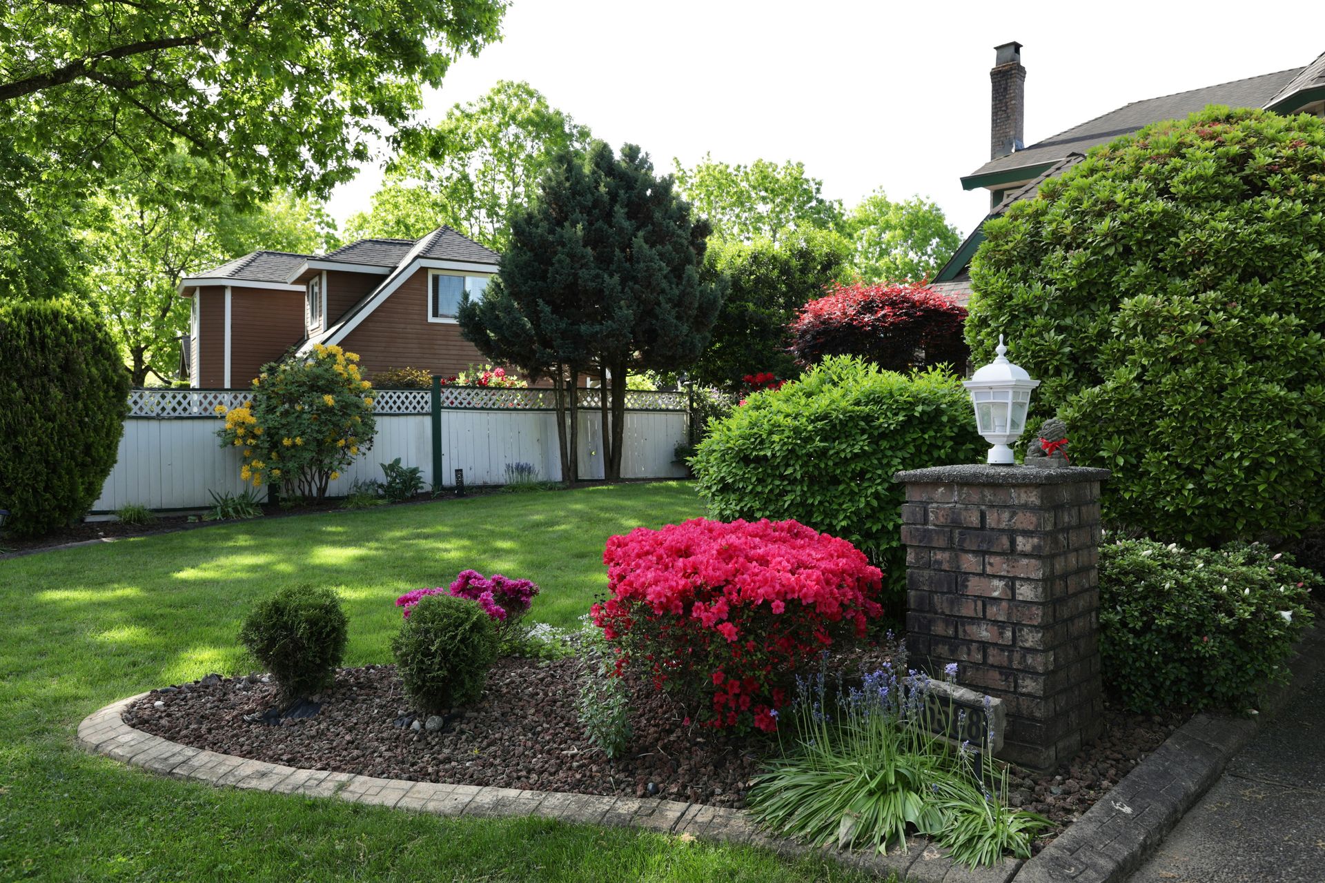 Lush green garden with blooming flowers and brick lamp post.